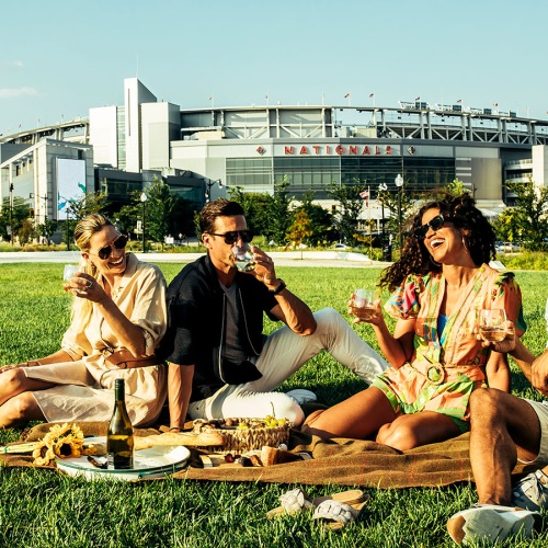 Close to the center of everything friends sit in a field in front of a stadium