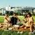 friends sit in a field in front of a stadium